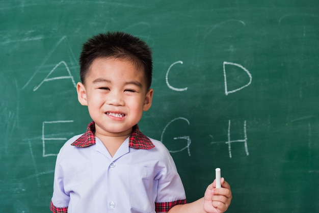 Asian little child boy kindergarten preschool smile in student uniform hold white chalk