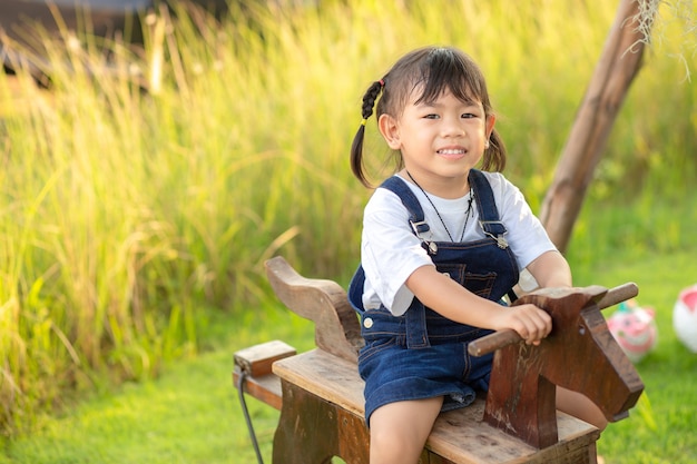 Asian little child girl riding on a wooden toy horse in the green grass garden.