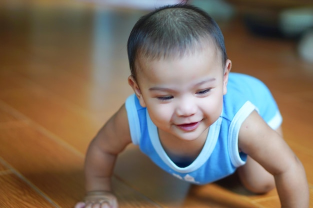 青いタンクトップを着たアジアの小さなかわいい赤ちゃんが這って幸せそうに笑っています