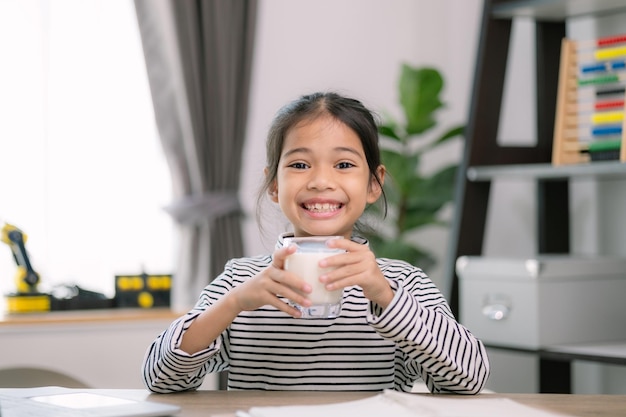 アジアの可愛い小さな女の子が牛乳を飲んでいる幼稚園児の女の子や娘は笑顔で家にいて幸せで牛乳を楽しんでいます