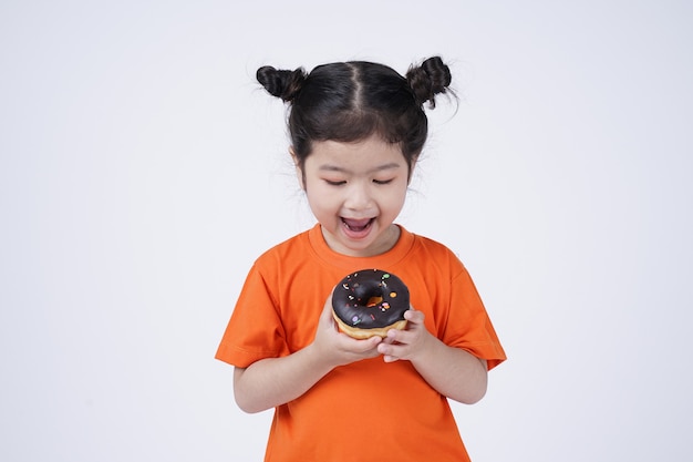 Piccola ragazza sveglia asiatica che mangia grande ciambella