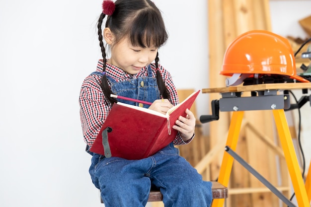 Asian little girl carpenter working on woodworking in carpentry shop Carpenter working on wood craft at workshop construction material wooden furniture Asian little girl works in a carpentry shop