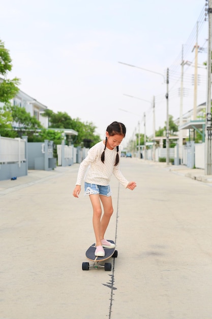 스케이트 보드에서 스케이트를 타는 아시아 소녀 아이 거리에서 야외에서 스케이트 보드를 타는 아이 그녀는 도로에서 스케이트 보드를 타고