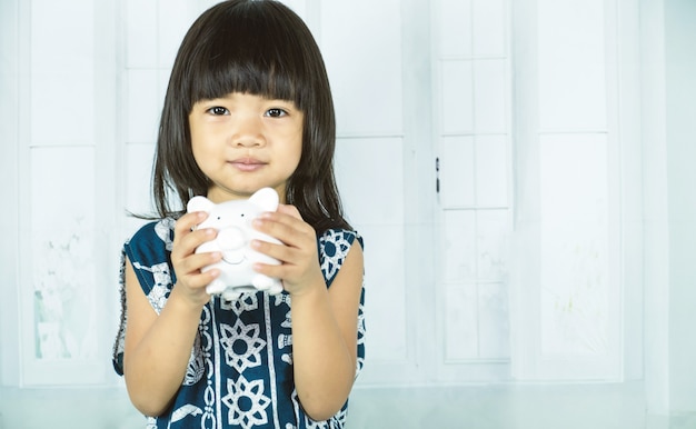 Asian little girl hand holding white piggy bank, learn to saving for the future concept.