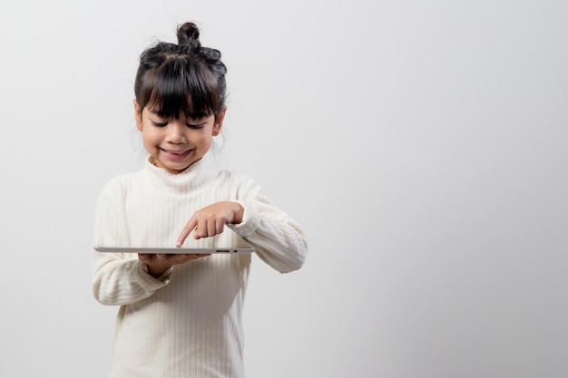 Азиатская маленькая девочка держит и использует цифровой планшет на белом фоне студии бесплатное пространство для копирования