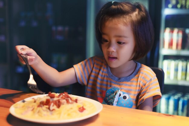 Asian little girl is eating spaghetti bolognese in the restaurant happily.