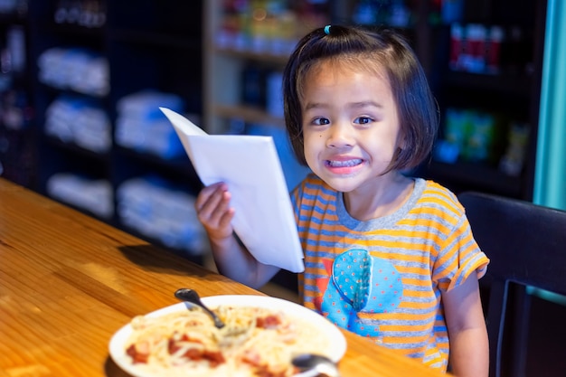 Азиатская маленькая девочка ест спагетти Болоньезе в ресторане счастливо.