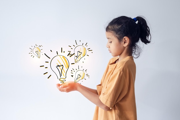 Азиатская маленькая девочка смотрит на руку с иконами лампочки о творчестве на сером фоне концепции идеи будущего