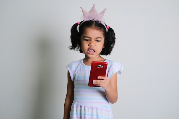 Asian little girl looking to her mobile phone with annoyed face expression