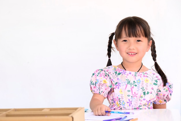 家の白い壁に就学前の子供のための紙の本で絵を描いたり、宿題を作って横たわっているアジアの少女
