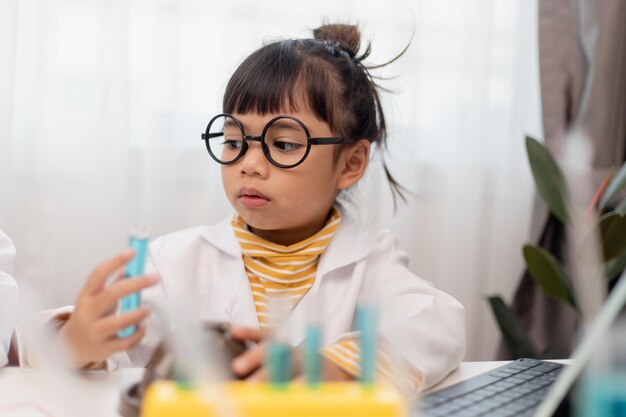 Bambina asiatica che misura la temperatura dell'acqua calda e fredda per una facile lezione online sperimentale di scienze