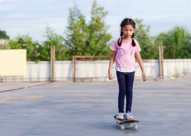 Азиатская маленькая девочка играет скейтборд и улыбка с счастье againts голубое небо