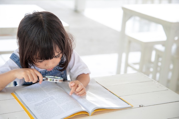 虫眼鏡で机の上の本を読んでアジアの少女