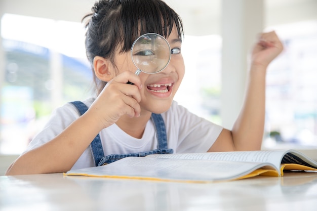 Asian Little girl reading the books on the desk with a magnifying glass