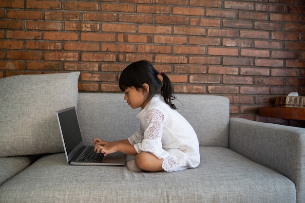 Asian little girl sitting on the couch having fun with laptop