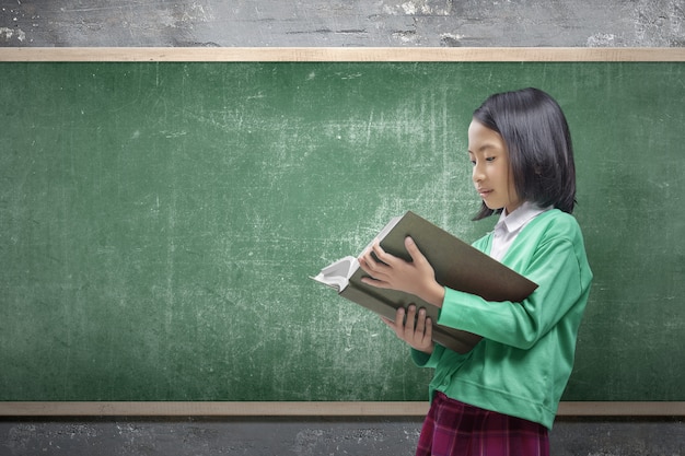 Asian little girl standing and reading the book in the classroom