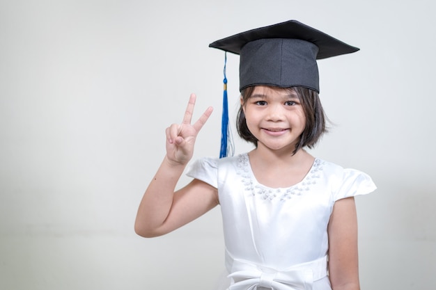 Asian little girl student wear a mortarboard or graduation hat hold a pencil and write on notebook