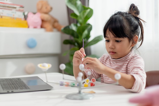 Asian Little girl studies the solar system in geography class looking at the scale model of planets