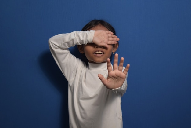 Asian little girl wearing white tshirt with her hand extended\
signaling to stop children violence