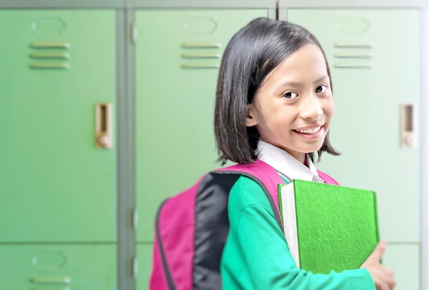 Азиатская маленькая девочка с книгой и рюкзаком в школе. Снова в школу концепции