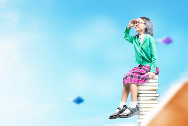 Asian little girl with eyeglasses sitting on the stack of books World Book Day