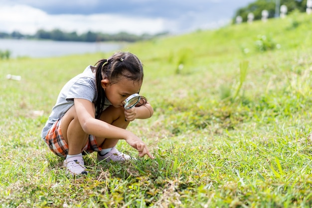 Asian little girl with magnifying glass looking for insects at meadow