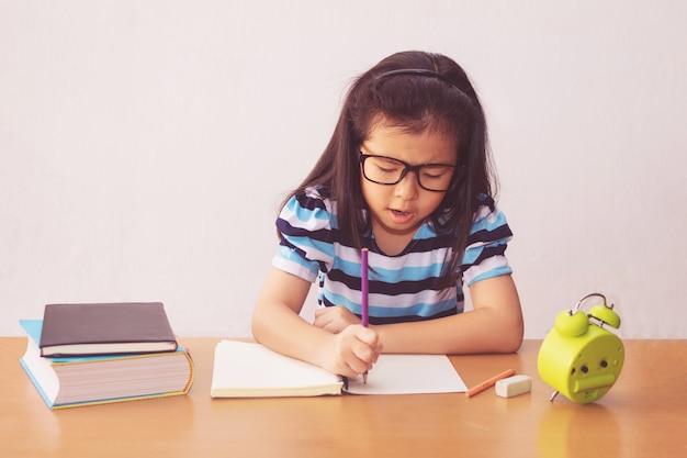 Bambina asiatica che scrive un libro sulla tavola