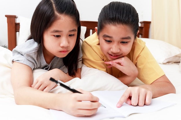 Bambine asiatiche che fanno i compiti insieme sul letto in camera da letto