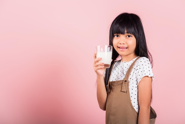 アジアの小さな子供10歳の笑顔はミルクグラスドリンクホワイトミルクを保持します