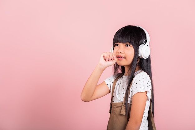 Asian little kid 10 years old smile listening music wear wireless headset and keeps hand near mouth sings song