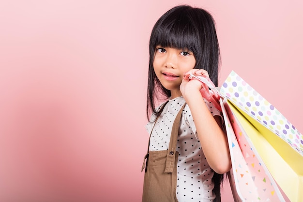 Asian little kid 10 years old smiling holding multicolor shopping bags in hands