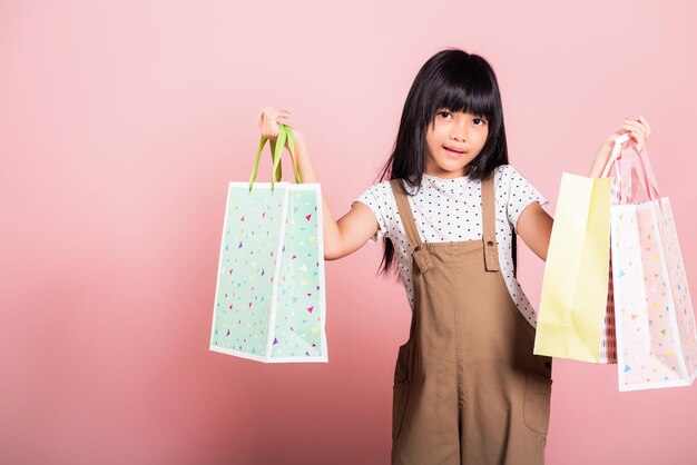 여러 가지 빛깔의 쇼핑백을 손에 들고 웃고 있는 10세 아시아 어린 아이