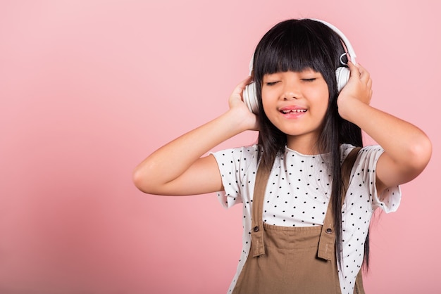 ワイヤレスヘッドセットを身に着けている音楽を聴いて笑っている10歳のアジアの小さな子供