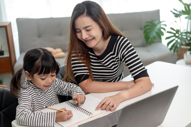 Asian little young girl kid learning online class at home with mother Preschool child use laptop computer do homework homeschool from school teacher by digital remote internet with support from mom