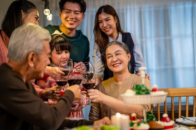 asian lovely family celebrating christmas party together in house attractive parents and relatives having dinner toasting a glass of wine to celebrate holiday thanksgiving xmas eve on dining table