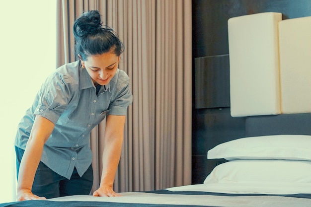 Asian maid making bed in hotel room