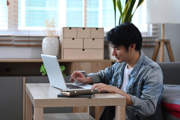 Asian male in casual wear working online with computer laptop in living room