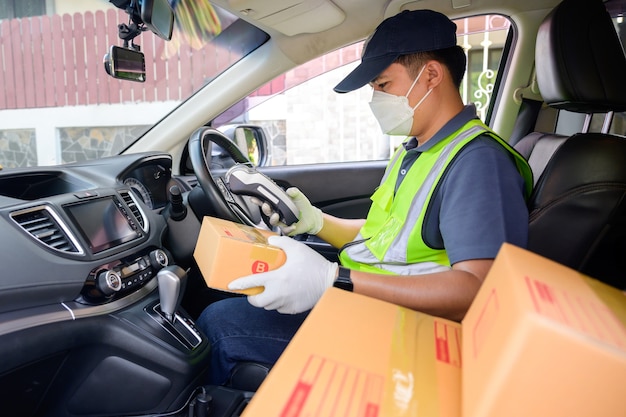 車の座席に段ボール箱と小包箱を持ったアジア人男性配達ドライバーが、コロナウイルスパンデミックCOVID-19の下でオンラインショッピングをしている顧客の配達を推進しています