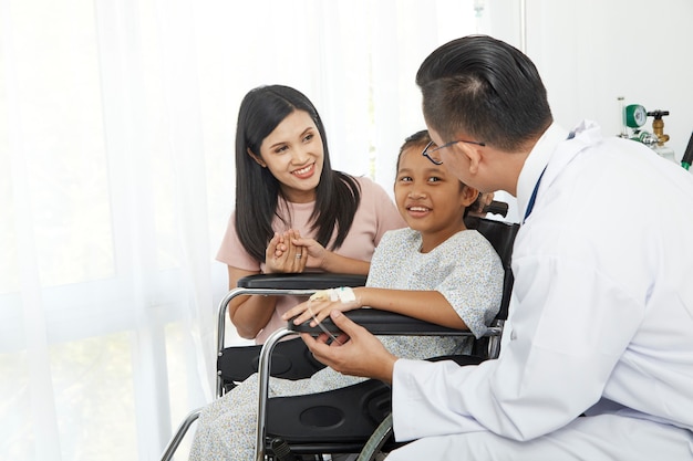 Asian male doctor talking to young child wheelchair and mother, Concept hospital care