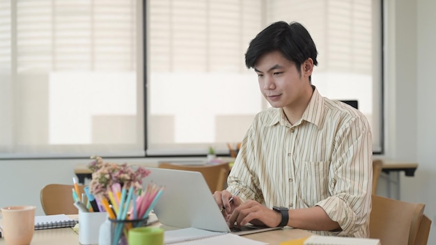 Asian male employee working with computer laptop at modern co working office space