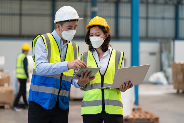 Asian male engineer in helmet safety wear mask to protect coronavirus discuss with female technician