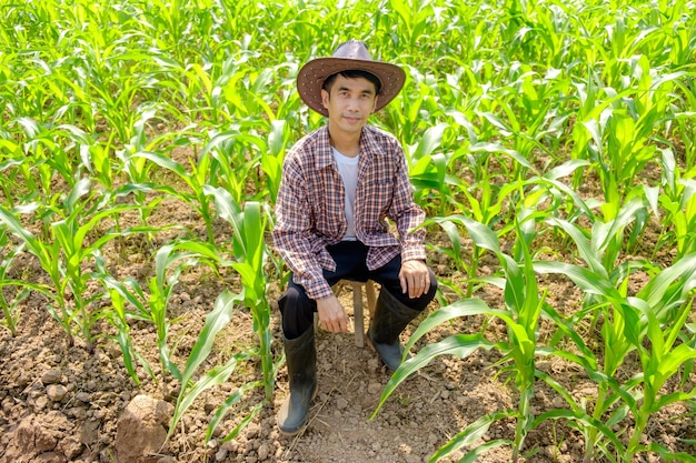 Asian male farmer in striped shirt and hat sitting at corn farm