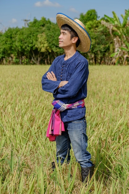 Asian male farmer wearing traditional blue dress standing with arms crossed Facing to the side at the farm