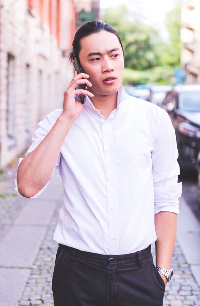 Asian male freelancer walking near business center holding phone, smiling reading news, successful b