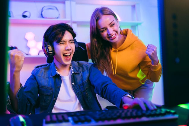 An Asian male gamer and Caucasian woman coach advice and discuss together in front of the gaming table Gamer winning an esports game with a mentor The player rejoices in victory in the competition