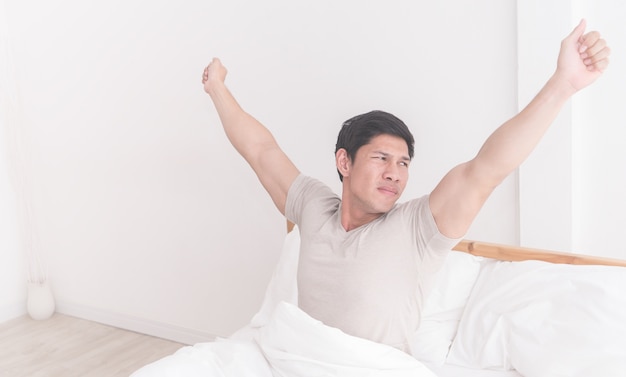 Азиатский мужчина растягивается после того, как проснулся на кровати