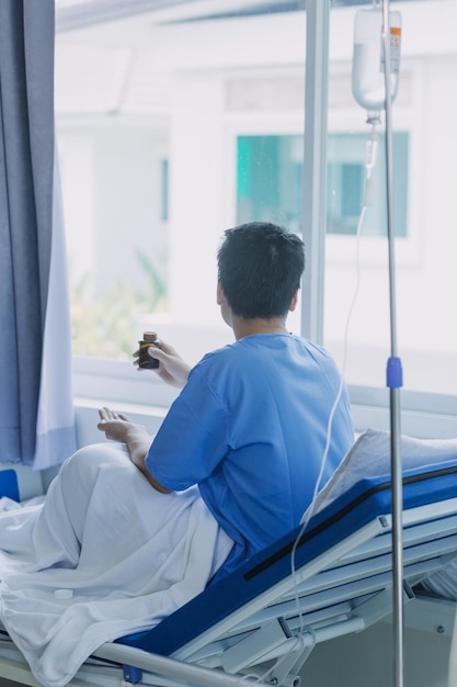 写真 アジア人の男性患者が病棟の回復室でフェイスマスクをしてベッドに横たわっているコロナウイルスのパンデミック中に、新型コロナウイルス感染症を防ぐために全員がマスクを着用している男性は孤独で退屈を感じている