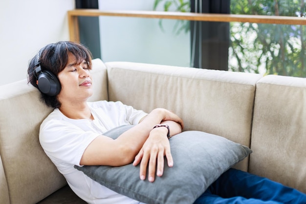自宅でヘッドフォンを付けてソファで休むアジア人男性 リラックスしてレジャー活動をする時間