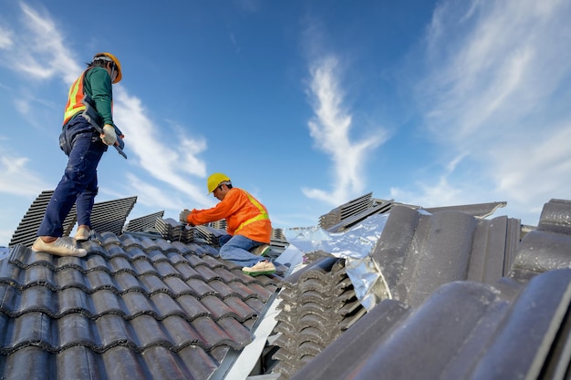 Asian male roof installer Asian construction workers on the roof Work using a drill bit to fix ceramic or cement roofing screws on the construction site