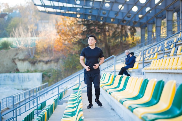 Maschio asiatico corridore che corre intorno al moderno stadio urbano su per le scale cardio mattina jog scalata rampicante uomo jogging all'aperto. allenamento sportivo uomo atleta a passi, in città. stile di vita sano fitness attivo